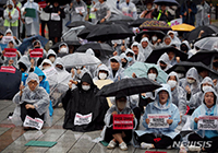 雨天の街頭で集会を開く不動産詐欺の被害者ら